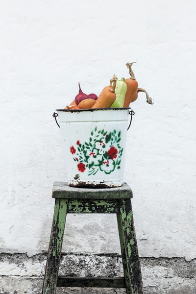 绿色木凳上的白色和五彩花桶中的蔬菜